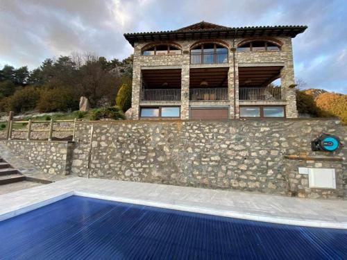 una casa con un muro in pietra e una piscina blu di Mas merolla casa para descanso familiar a Gombreny