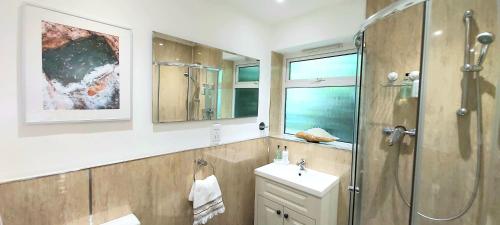 een badkamer met een douche, een wastafel en een spiegel bij Kindly Light Beach House in Porthmadog