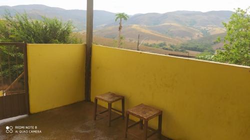two stools sitting on a balcony with a yellow wall at Casa de Temporada Serra da Canastra - São Roque de Minas in São Roque de Minas