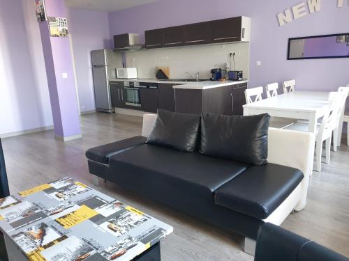 un salon avec un canapé noir et une cuisine dans l'établissement Villers sur Mer - Cocon familial, détente, évasion, vue sur mer, à Villers-sur-Mer