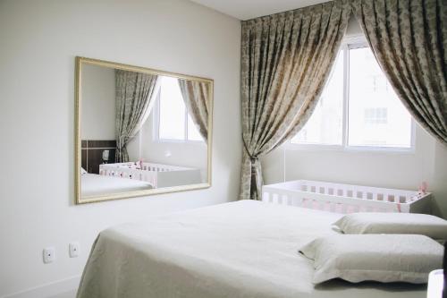Dormitorio blanco con espejo grande y cama en Apartamento em Itapema a 400m do mar, en Itapema