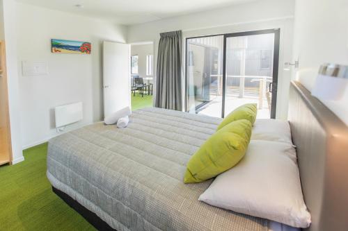 ein Schlafzimmer mit einem Bett mit gelben Kissen und einem Balkon in der Unterkunft Camp Waipu Cove in Waipu