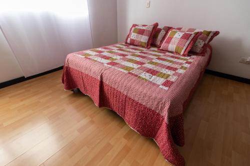 a bed with a quilt and pillows in a room at Milán, Acogedor apto en Zona Rosa con Balcón in Manizales