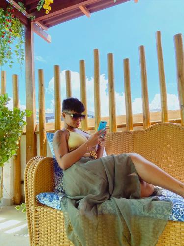 a woman sitting in a wicker chair looking at her cell phone at Pousada Capital das Águas in Maceió