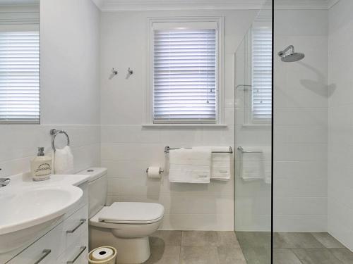 a white bathroom with a toilet and a glass shower at Old Bank Stables in Moss Vale