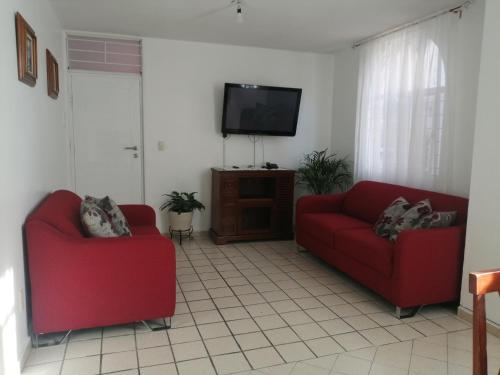 a living room with two red chairs and a flat screen tv at Departamento centrico cerca de la feria in Aguascalientes