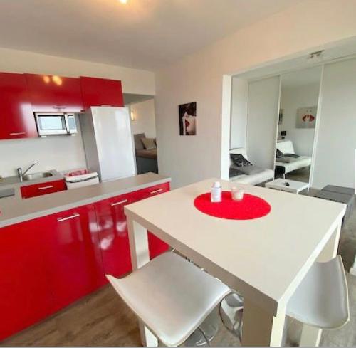 une cuisine avec des placards rouges et une table blanche avec des chaises dans l'établissement NATURA LOFT, au Cap d'Agde