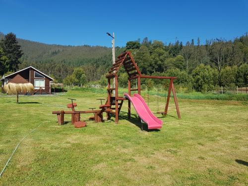 a playground with a slide and a swing at Cabañas Los Cipreses in Contulmo