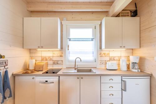 a kitchen with white cabinets and a sink and a window at Domki nad morzem Otulone Słońcem in Rowy