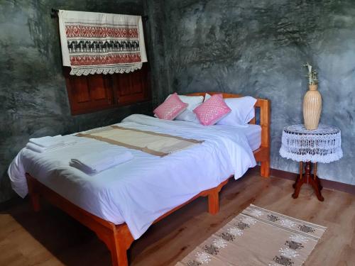 a bedroom with a bed with white sheets and pink pillows at เฮือนไม้ชมนาด Huanmaichommanard in Chiang Mai