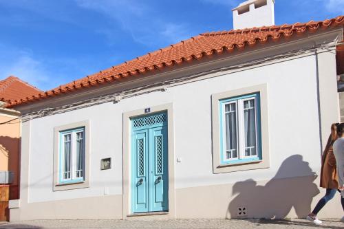 a woman walks past a small white house with a blue door at Heritage House Leiria in Leiria