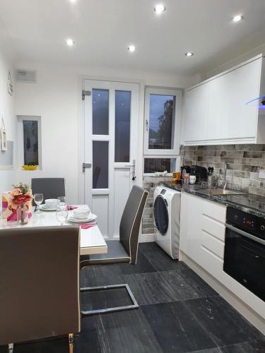 a kitchen with white cabinets and a table with chairs at Glasgow Comfortable and Modern 3 Bedroom Mid Terraced Villa in Glasgow