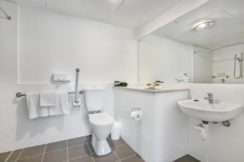 a white bathroom with a toilet and a sink at Shellharbour Village Motel in Shellharbour