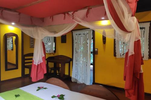 a room with yellow walls and a bed with curtains at Clair de Lune in Ambatoloaka