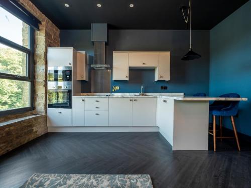 a kitchen with white cabinets and a blue wall at Bowers Mill Aparthotel in Barkisland
