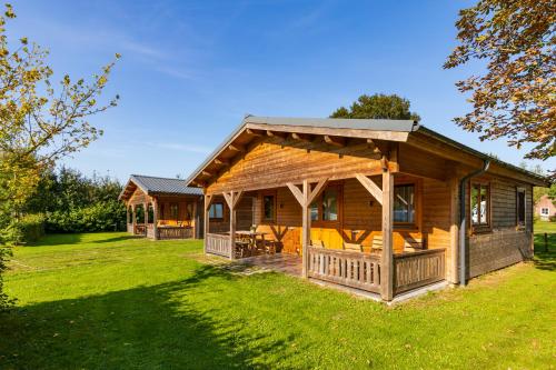 a log cabin with a porch and green grass at Vakantiehuis De Schaapskooi in Drunen