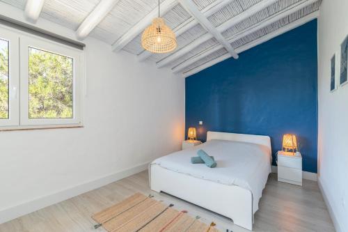 um quarto com uma cama branca e uma parede azul em Palmeiras Cottages em Mexilhoeira Grande