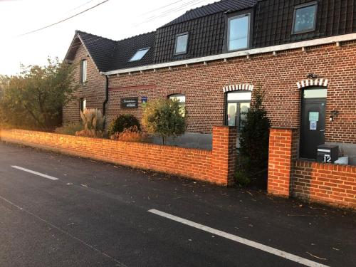 ein Backsteinhaus mit einem Steinzaun neben einer Straße in der Unterkunft Aux Herbes Hautes in Fleurbaix