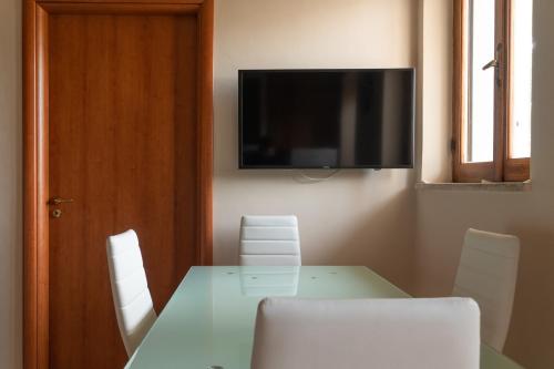 une table avec des chaises blanches et une télévision murale dans l'établissement Bougainvillea casa vacanza, à Castelbuono