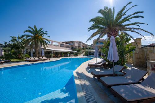 a swimming pool with lounge chairs and a palm tree at Isida Hotel Agia Marina in Agia Marina Nea Kydonias