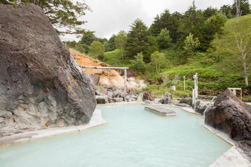 a pool of blue water next to a large rock at Manza Kogen Hotel in Tsumagoi