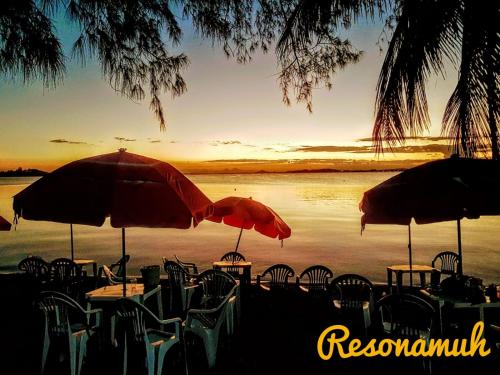 a group of tables and chairs with umbrellas on a beach at RESONAMUH - Hostel in São Pedro da Aldeia