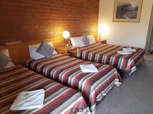 three beds in a hotel room with towels on them at All Rivers Accommodation in Echuca
