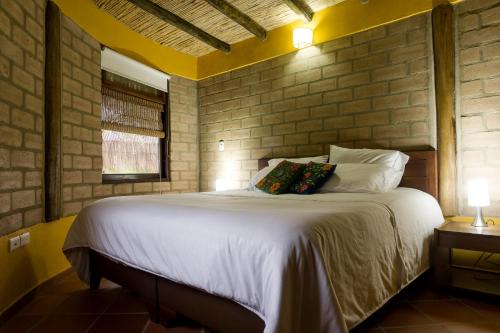 a bedroom with a white bed with a brick wall at Cabaña Campestre Sol Muisca RNT85322 in Villa de Leyva