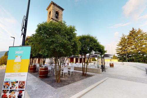 a building with a clock tower with tables and trees at Conca Bella Boutique Hotel & Wine Experience in Vacallo