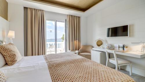 a hotel room with a bed and a desk and a window at Hotel Illa d'Or & Club Apts 4* Sup in Port de Pollensa