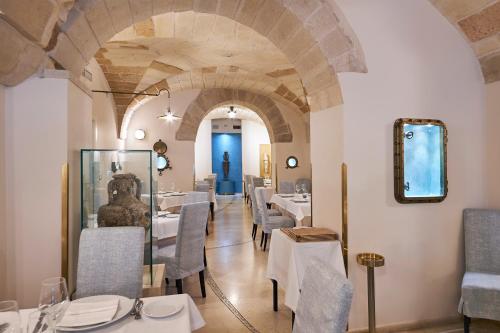 un ristorante con tavoli e sedie bianchi e un arco di Corte Di Nettuno - CDSHotels a Otranto