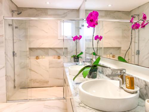 uma casa de banho com 2 lavatórios e um chuveiro com flores cor-de-rosa em Casa com 4 suítes em Jurerê Internacional em Florianópolis