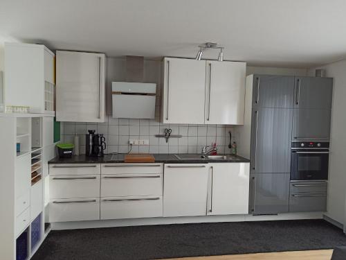 una cocina con armarios blancos y electrodomésticos de acero inoxidable en Fewo Höhbergblick en Tauberbischofsheim