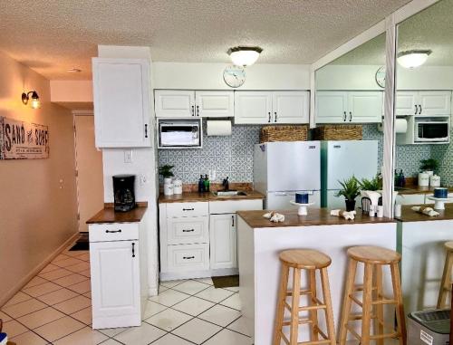 una cocina con armarios blancos y taburetes de bar en Beach Daze - Ocean front at Symphony Beach Club!, en Ormond Beach