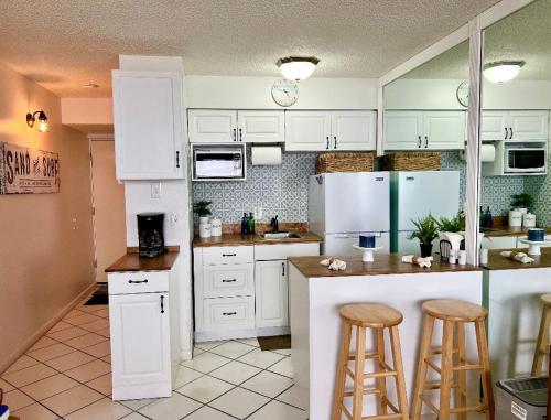 a kitchen with white cabinets and bar stools at Beach Daze - Ocean front at Symphony Beach Club! in Ormond Beach