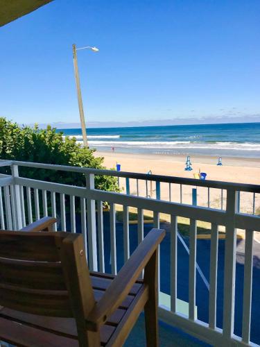 a wooden chair sitting on a balcony overlooking the beach at Beach Daze - Ocean front at Symphony Beach Club! in Ormond Beach