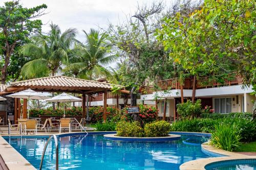 a pool at a resort with tables and umbrellas at Village Enseada Ville, Itacimirim, Bahia in Itacimirim