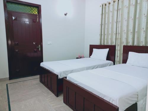 two twin beds in a room with a door at Cosy Inn Guest House in Karachi