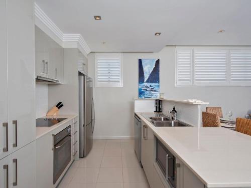 a white kitchen with a sink and a refrigerator at Aura Apartments Unit 12 59 Shoal Bay Road in Shoal Bay