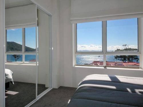 a bedroom with a bed and windows with a view of the ocean at Barrington, 707/35-45 Shoal Bay Road in Shoal Bay