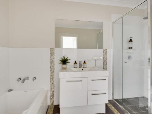 een witte badkamer met een douche en een wastafel bij Sea Breeze On Carroll in Mollymook