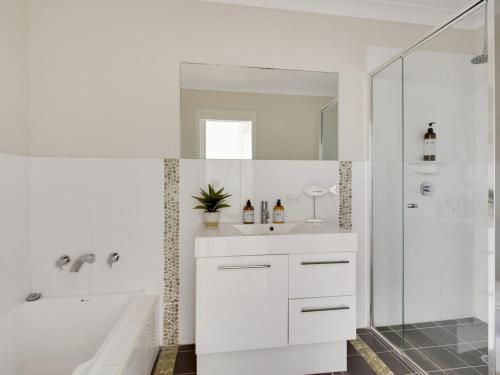 a white bathroom with a shower and a sink at Sea Breeze on Carroll - 4BR beachside home in Mollymook