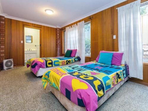 two beds in a room with wooden walls and windows at Marine Drive 32 in Fingal Bay