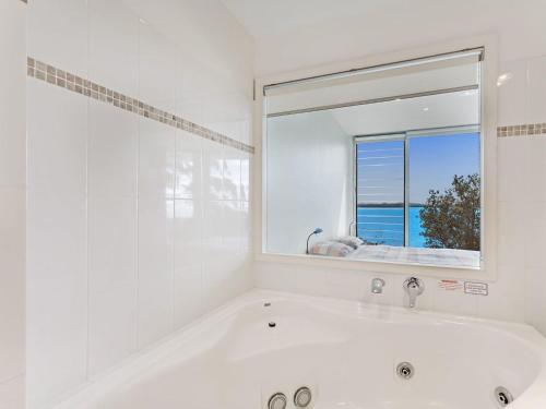 La salle de bains blanche est pourvue d'une baignoire et d'une fenêtre. dans l'établissement Mirage 1 24 Gloucester Street, à Nelson Bay