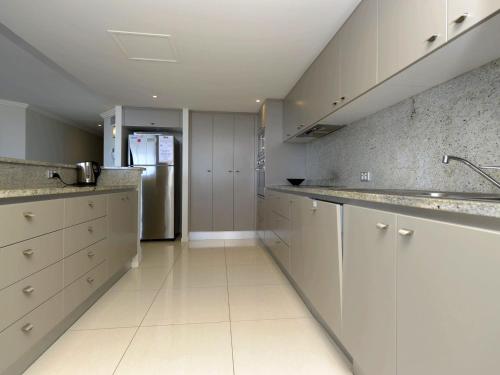 La cuisine est équipée de placards blancs et d'un réfrigérateur en acier inoxydable. dans l'établissement Oasis Unit 9 5 Laman Street, à Nelson Bay
