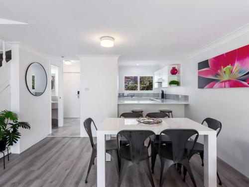a white dining room with a white table and black chairs at Pacific Blue Townhouse, 351/265 Sandy Point Road in Salamander Bay