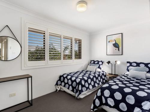 a bedroom with two beds and a mirror and windows at Pacific Blue Townhouse, 351/265 Sandy Point Road in Salamander Bay