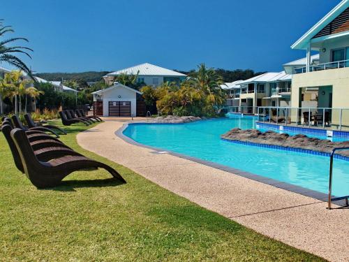 a row of benches sitting next to a swimming pool at Pacific Blue Townhouse, 351/265 Sandy Point Road in Salamander Bay