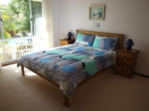 a bedroom with a bed with a colorful comforter and a window at Pacific Drive 89 in Fingal Bay