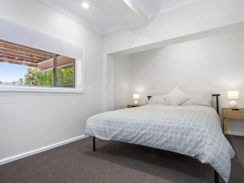 a white bedroom with a bed and a window at Fairwater In Mollymook in Mollymook
